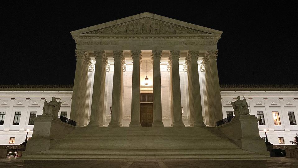 the front of the U.S. supreme court building lit up at night