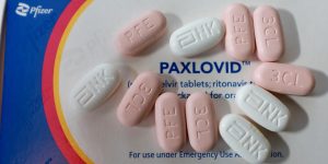 box of paxlovid with white and pink versions of pill scattered on top